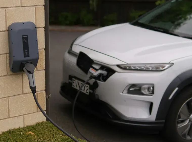 Wall mounted EV charger installed beside a driveway, charging an electric SUV